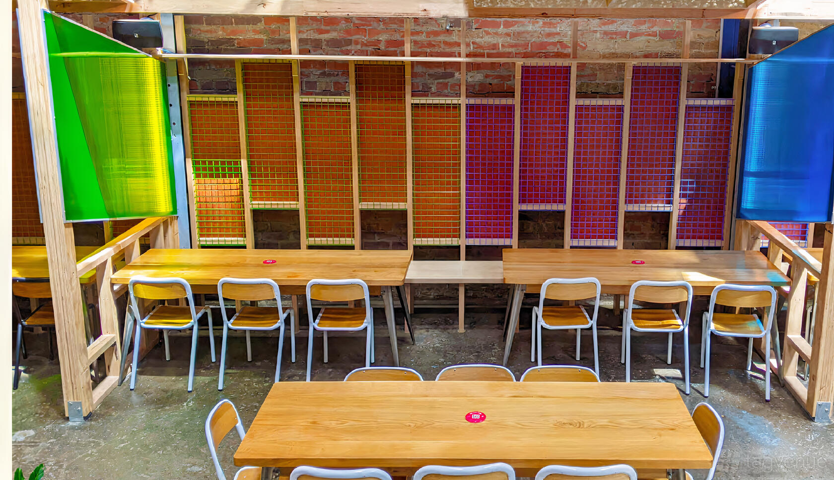 An event space with long wooden tables, metal chairs, and colorful wall panels at Co-Conspirators Brewpub.