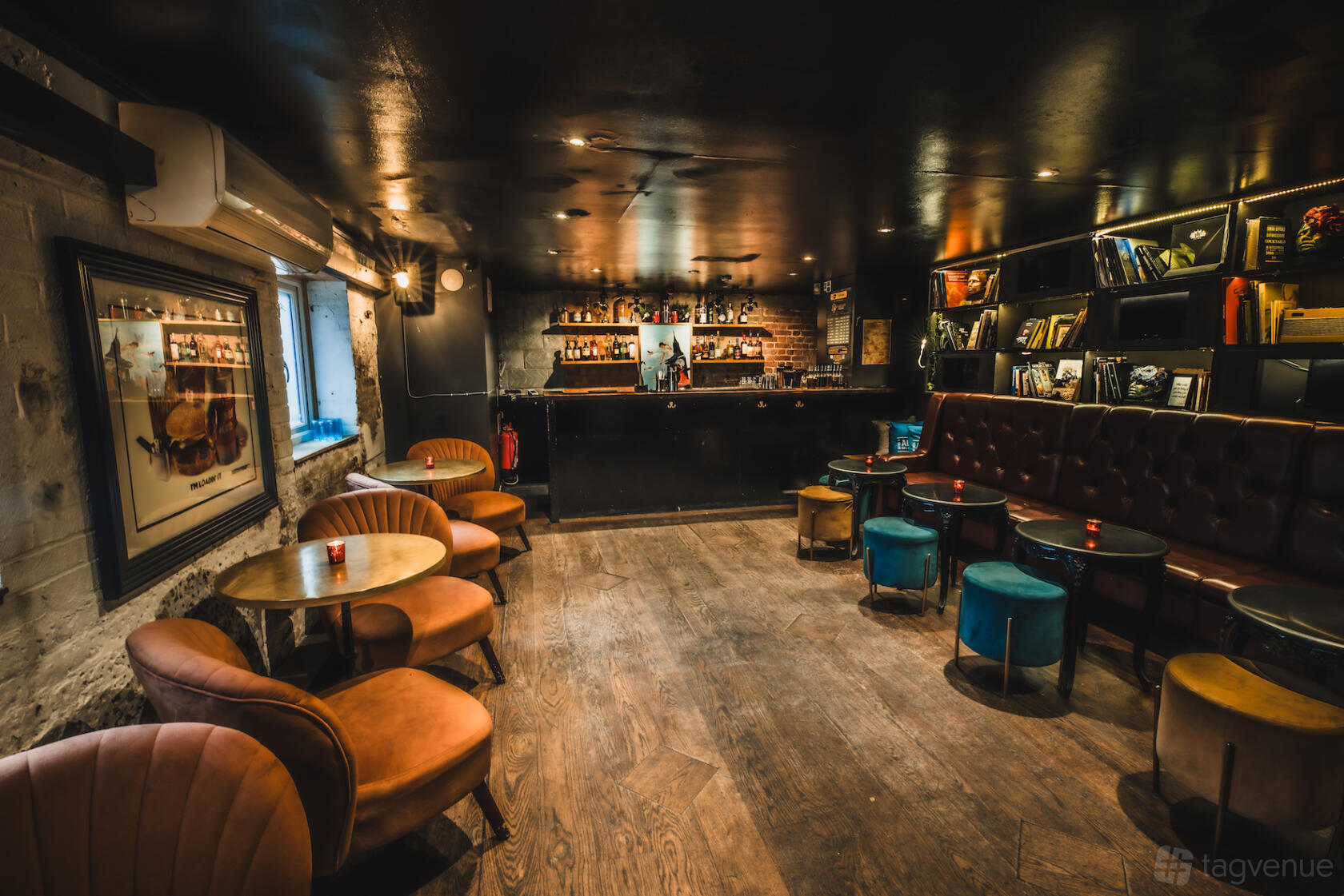 A function room in a cocktail bar with leather chairs, small round tables, exposed brick, and a stocked bar at Callooh Callay Shoreditch.
