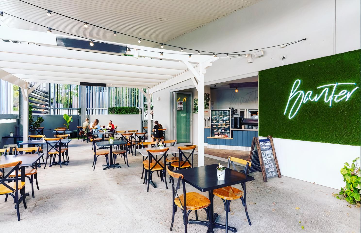 An open-air cafe patio with wooden tables, string lights, and a neon sign at Banter Coffee House.