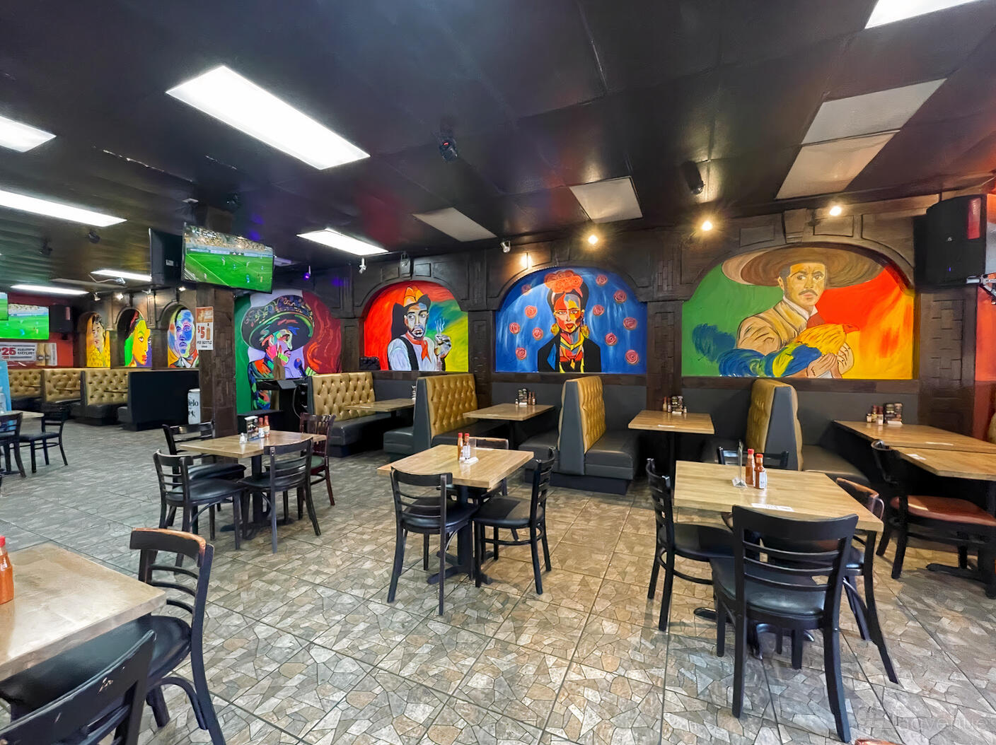 A restaurant with colorful mural art, booth seating, and wooden tables at Delicias De Mexico.