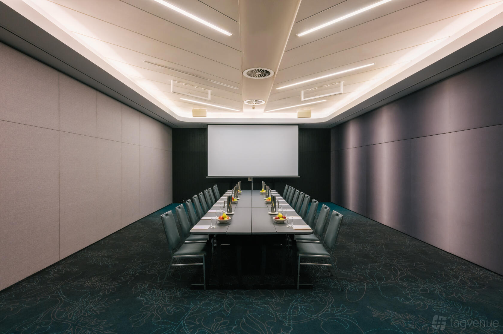A hotel function room with a long conference table, green chairs, and a ceiling-mounted projector at PARKROYAL Darling Harbour, Sydney.