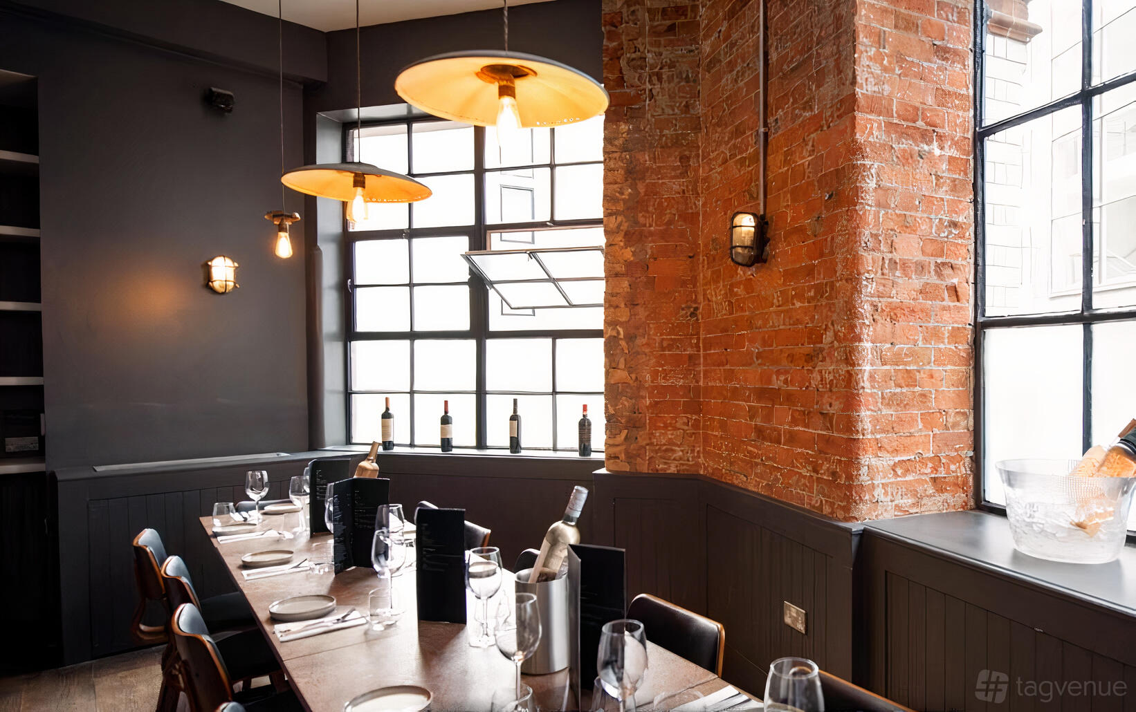 A restaurant dining room with exposed brick walls, large industrial windows, and a set table at Brix Ldn.