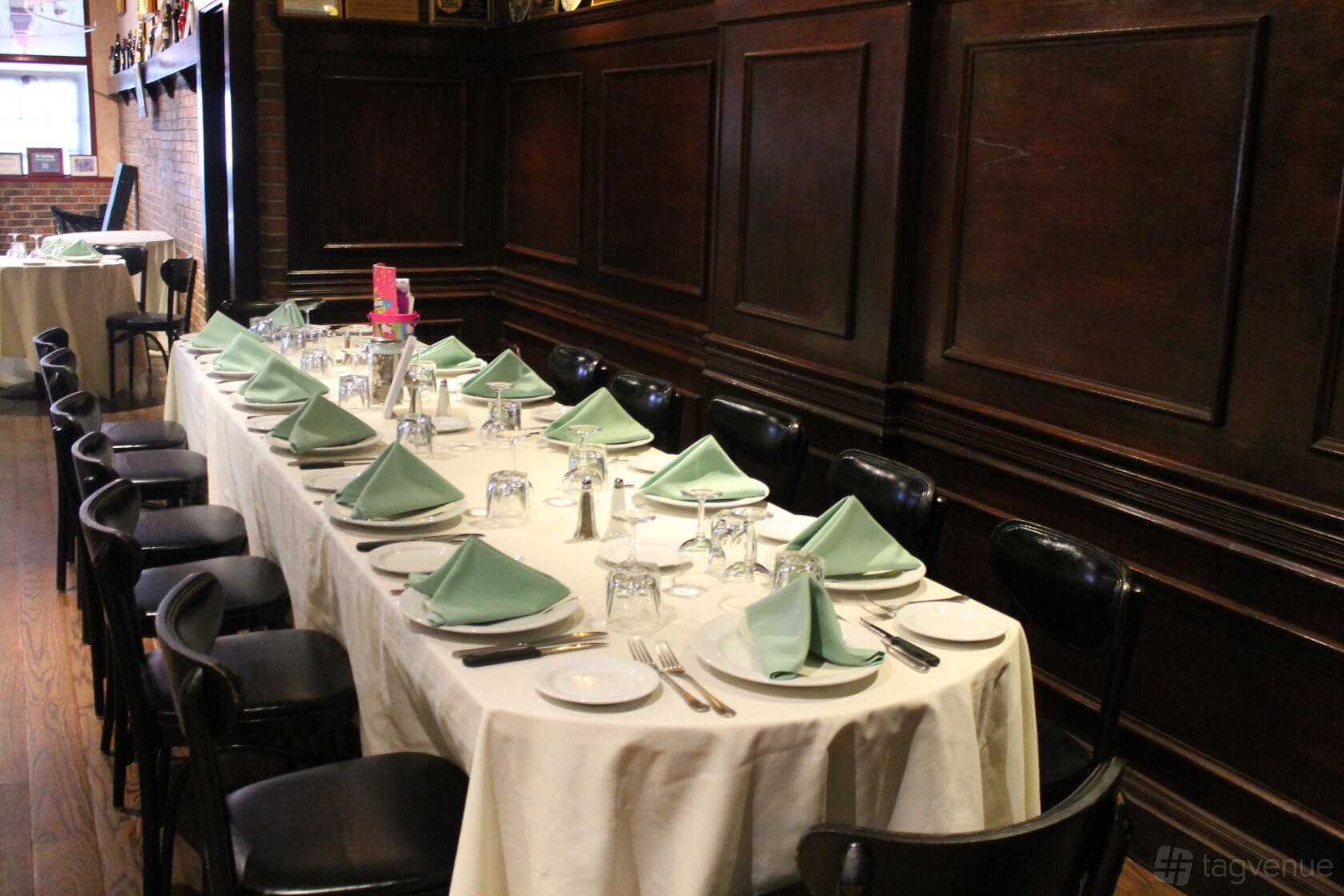 A restaurant with dark wood paneling, long table set with green napkins and white linens at Papazzio.