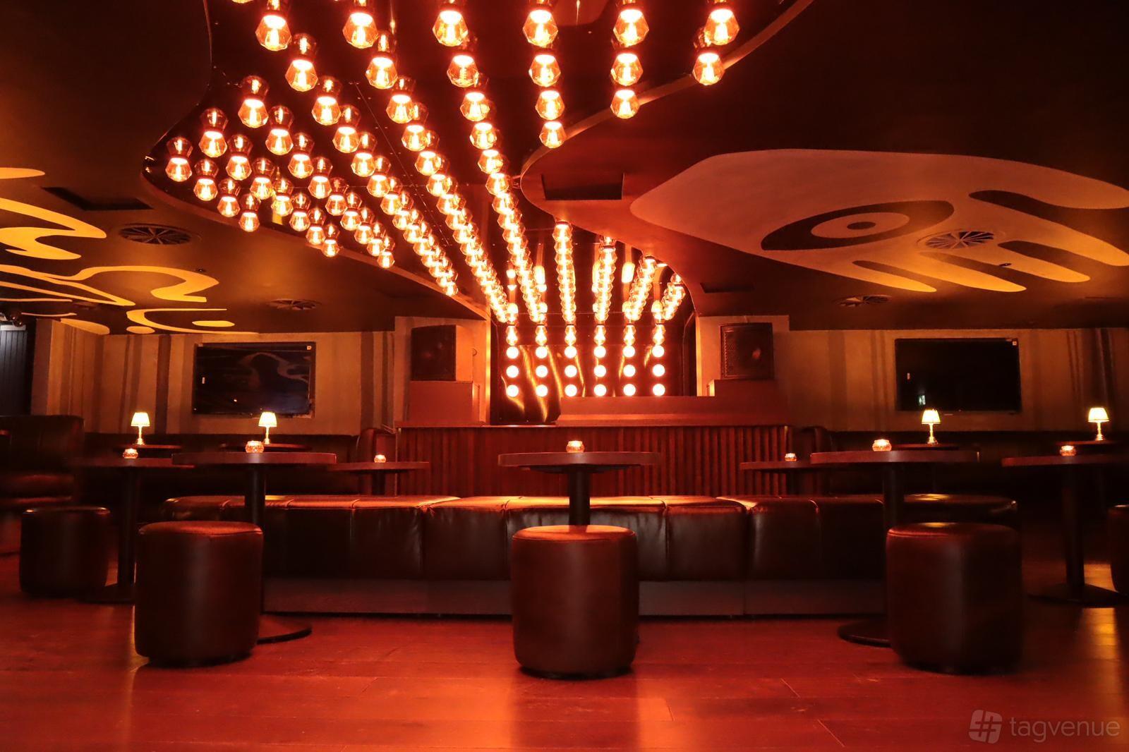 A bar with rows of low tables, leather seating, and warm ceiling lights at Coco.