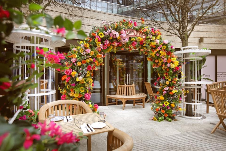 An outdoor pub area with wooden benches and a floral archway at Mr Fogg's City Tavern