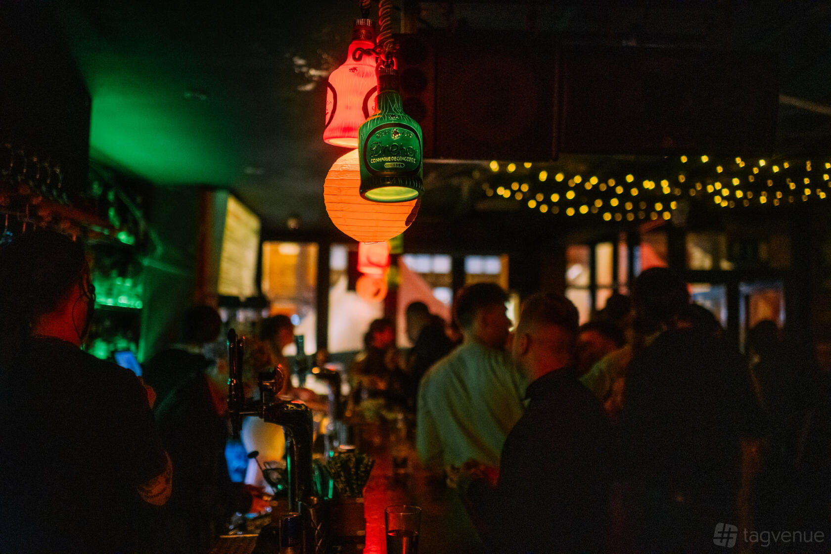 An underground bar with colorful lanterns, hanging glassware, and string lights above a busy counter at Verve Leeds.