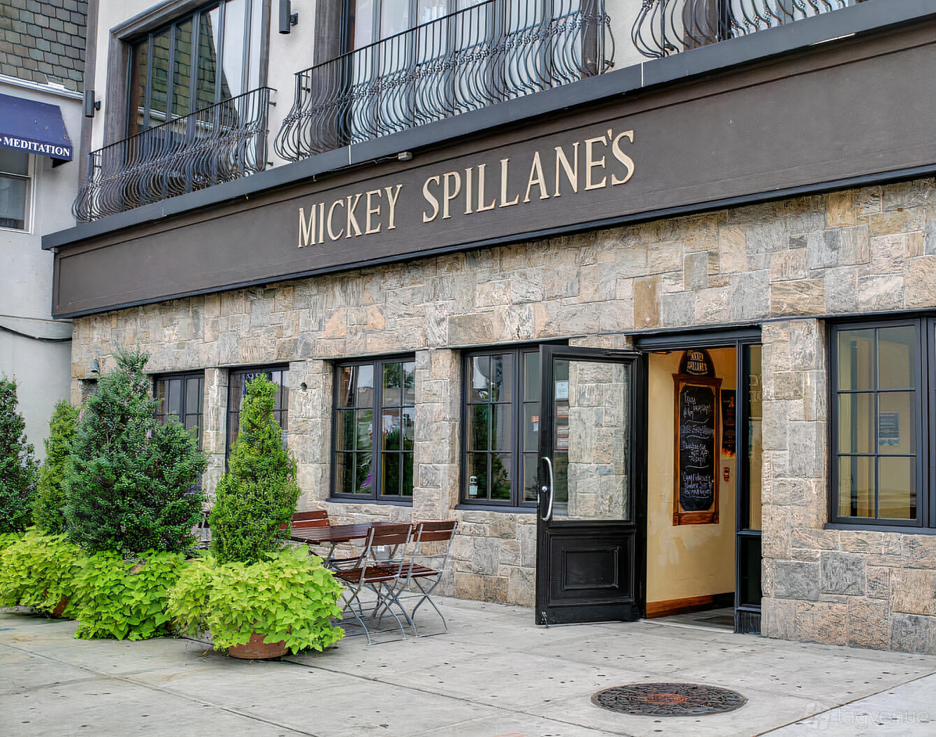 A pub with stone exterior walls, black framed windows, and outdoor seating with wooden tables at Mickey Spillane's.
