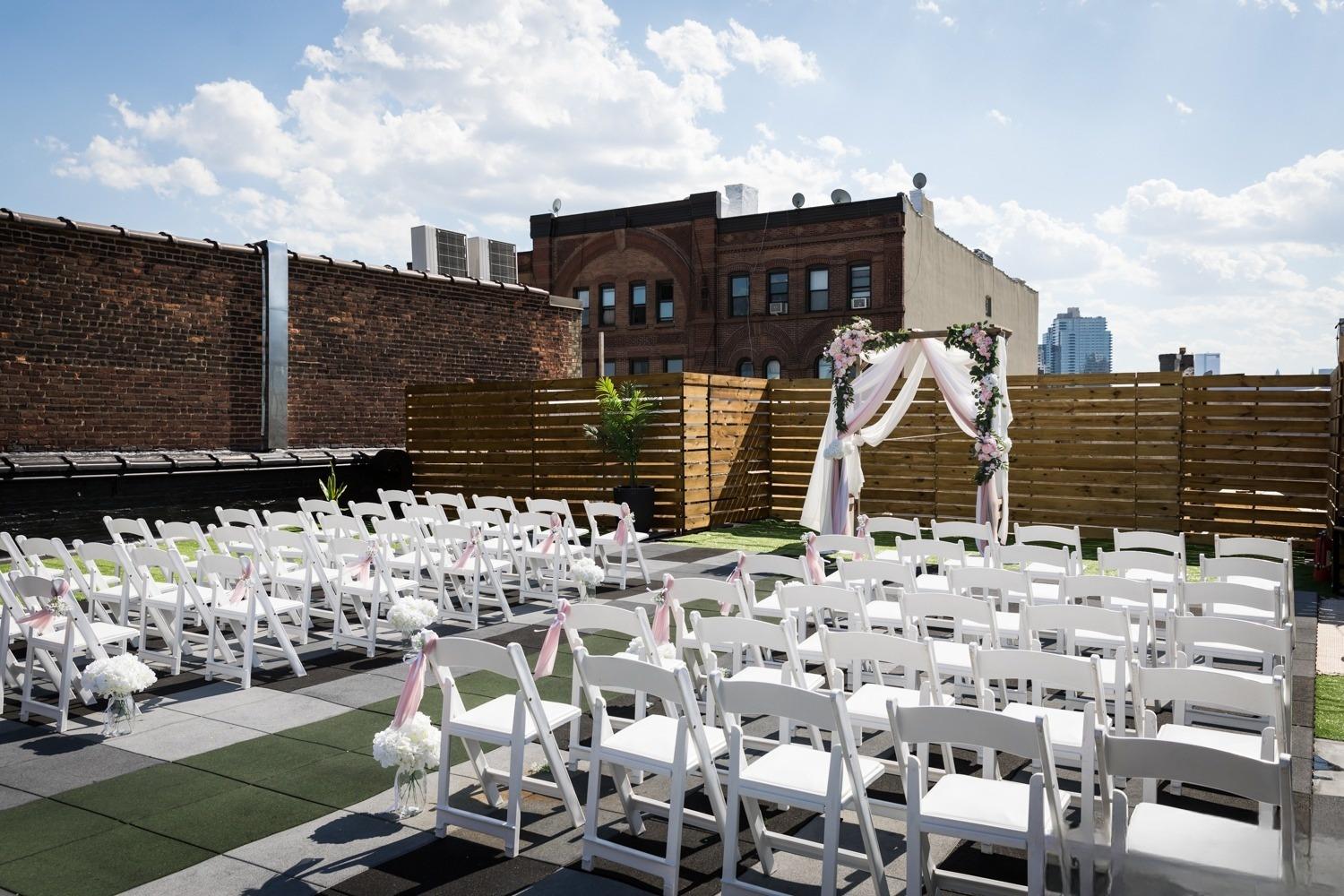 A rooftop event space with white folding chairs, a floral wedding arch, and city views at Loft Story Events.