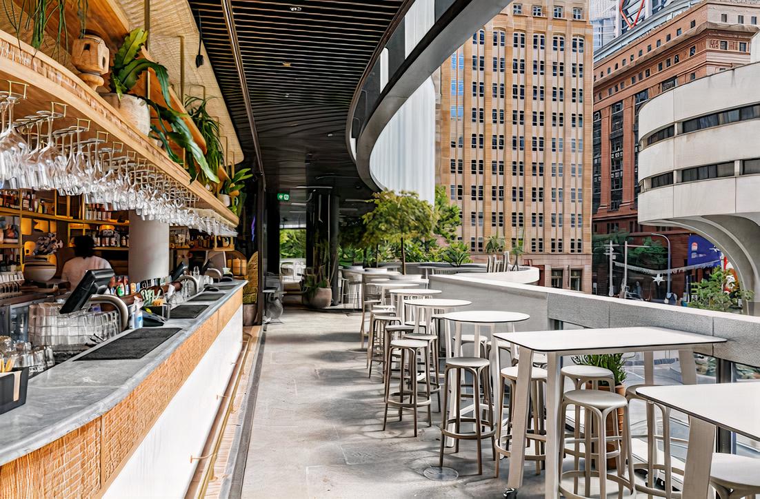 A bar with a long marble counter, overhead glass racks, high tables, and city views at Cabana Bar.