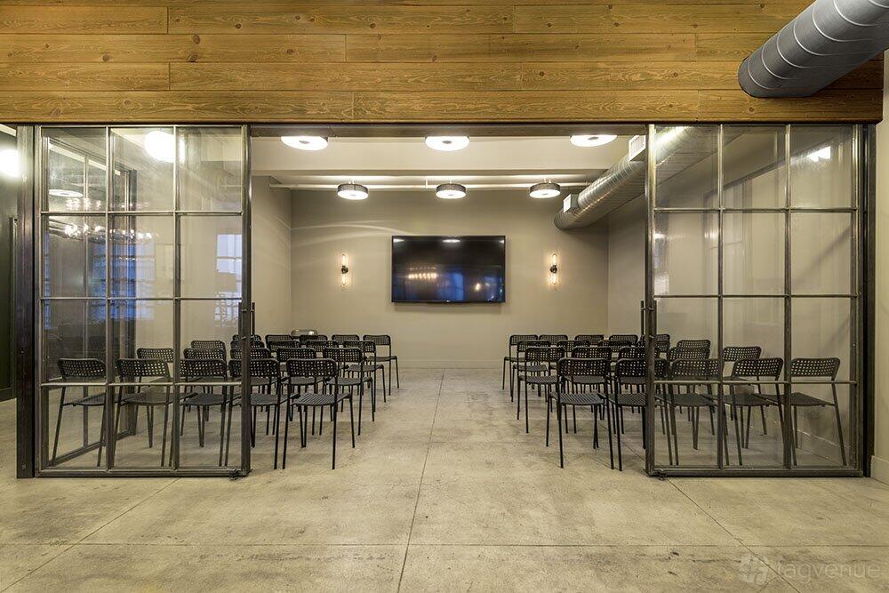 A screening room with rows of black chairs facing a wall-mounted TV screen and exposed ductwork at WorkHouse NYC - Midtown.