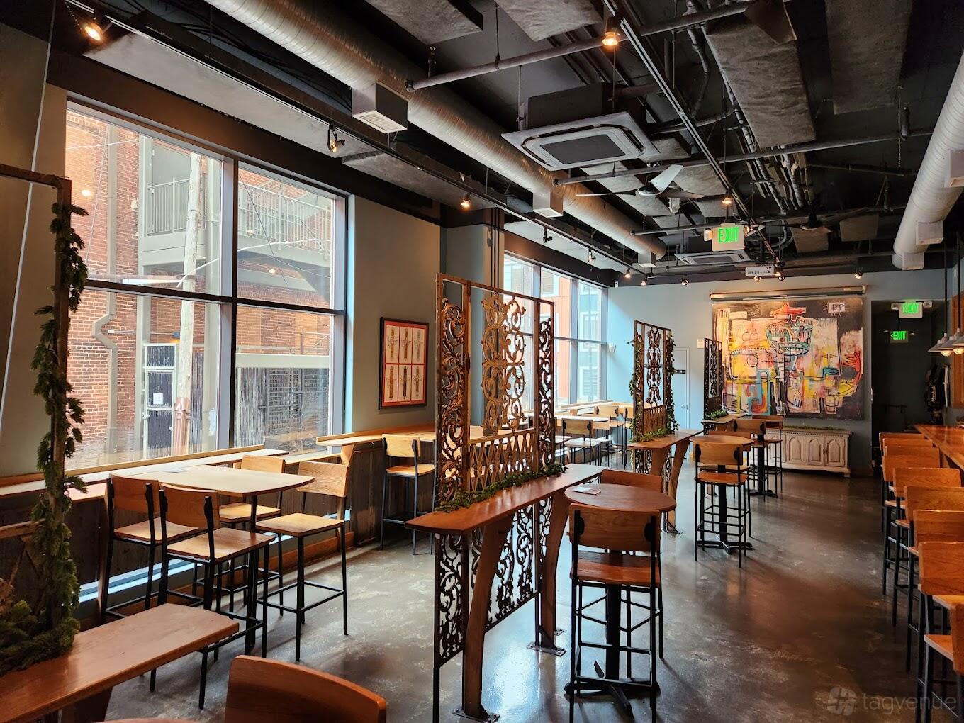 An event space in a restaurant with tall windows, wooden tables, and decorative metal dividers at Right Proper Brewing Company.