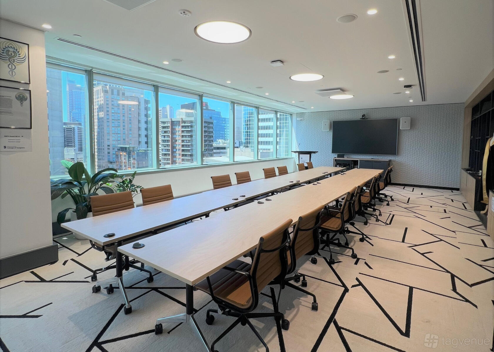A boardroom with a long conference table, ergonomic chairs, floor-to-ceiling windows, and city views at Royal Australasian College of Surgeons.