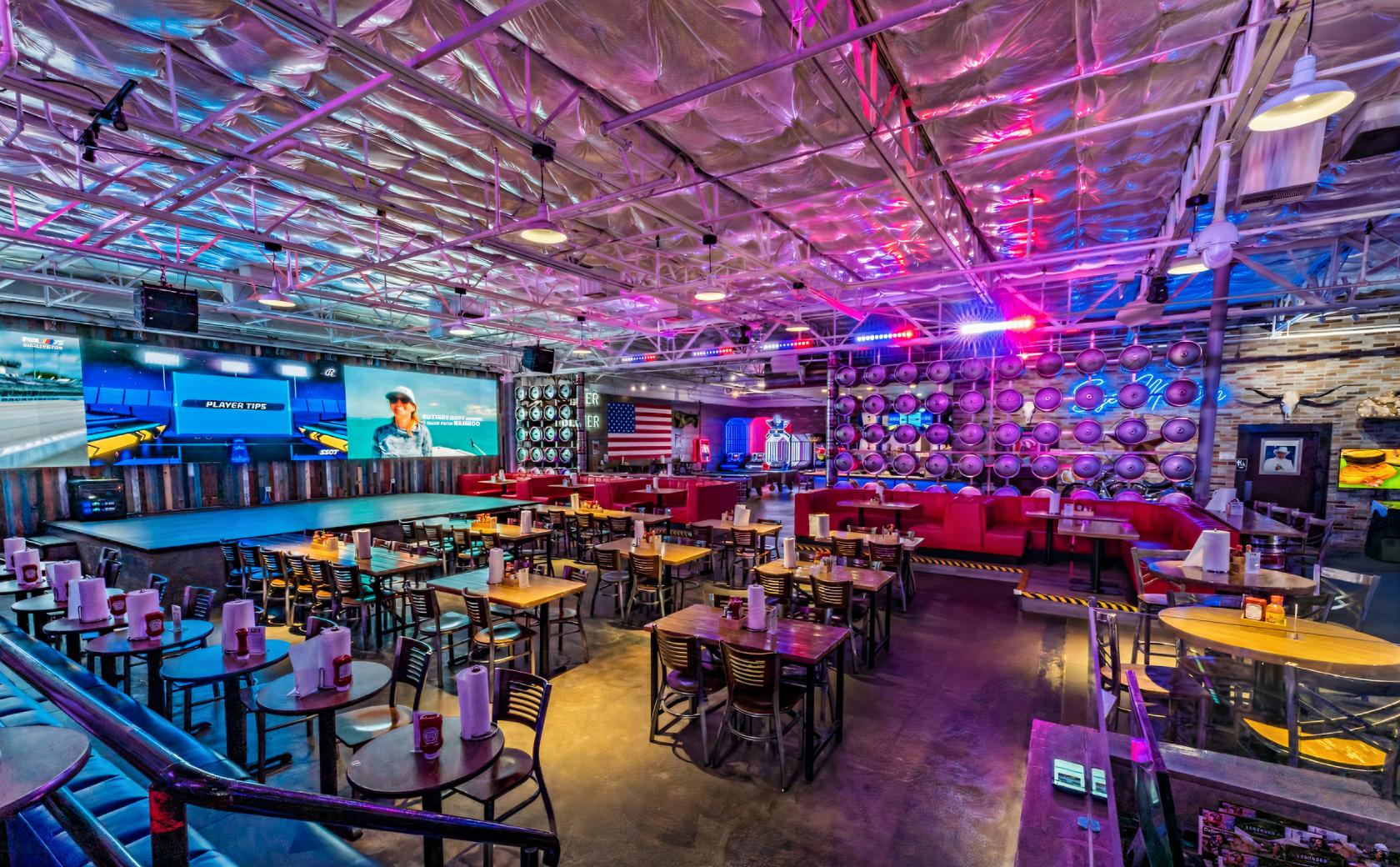 An event space in a bar with high-top tables, red booth seating, keg wall decor, and large video screens at Longhorn Icehouse.