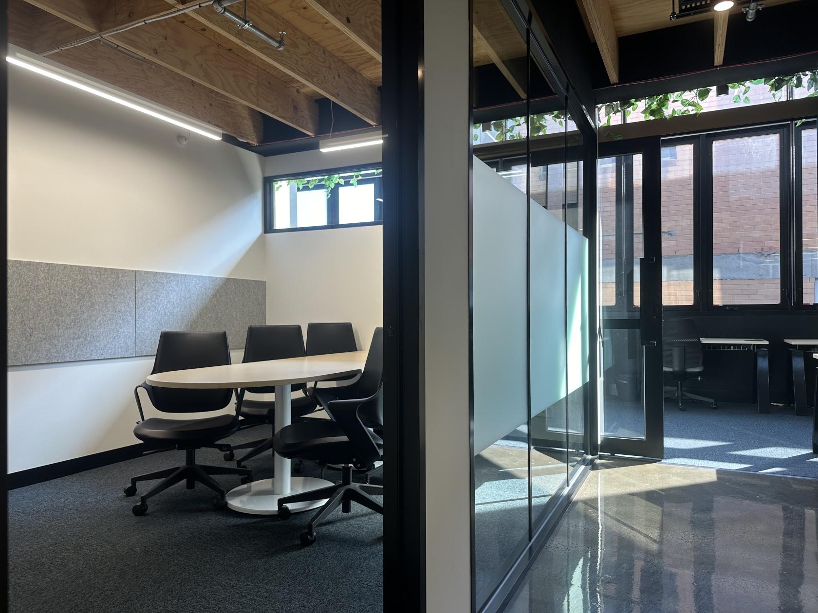 An office space with a round table, black swivel chairs, and large windows at collective_100.