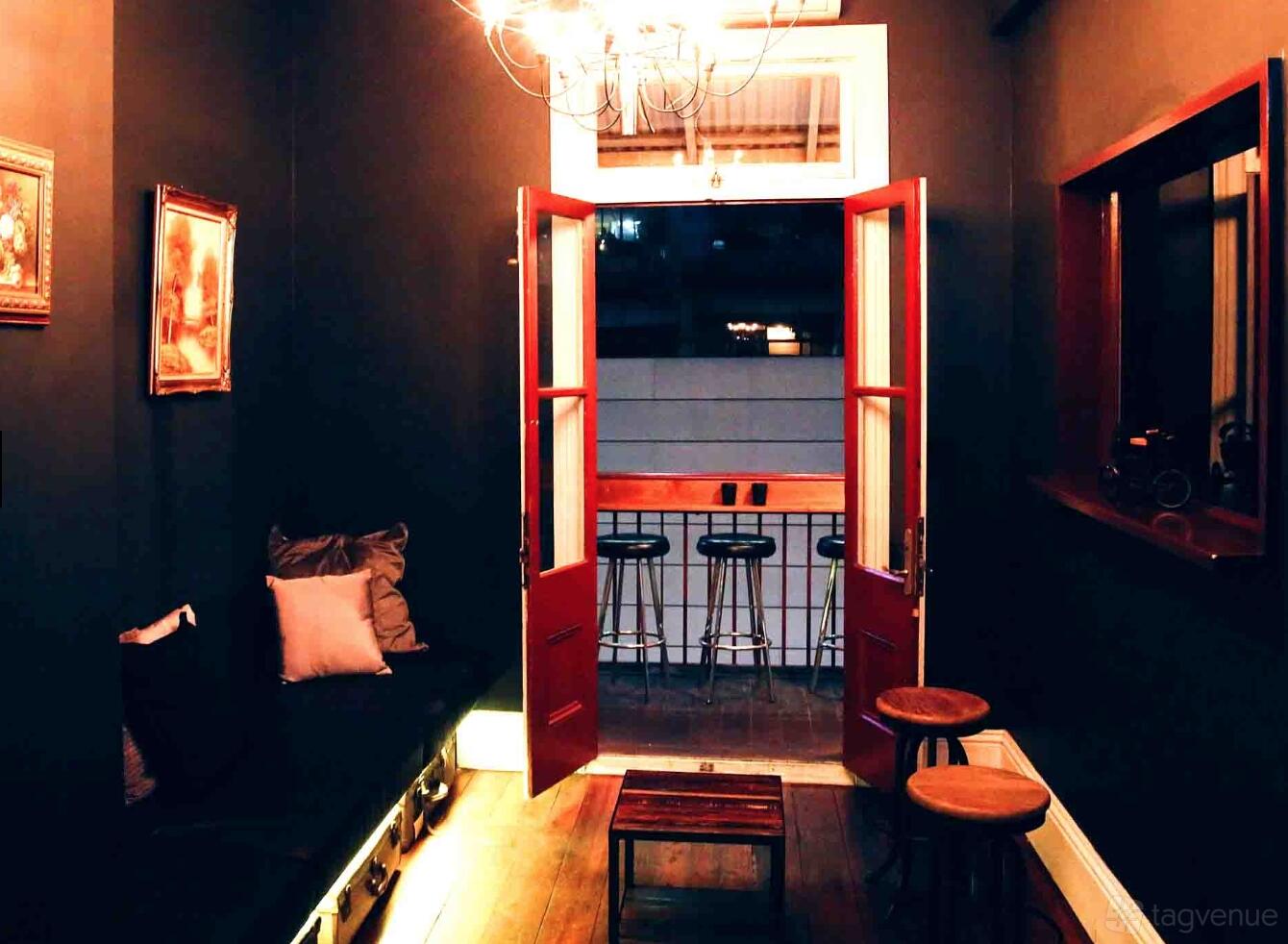 An event space in a bar with dark walls, cushioned bench seating, and a balcony with high stools at The Captain's Balcony.