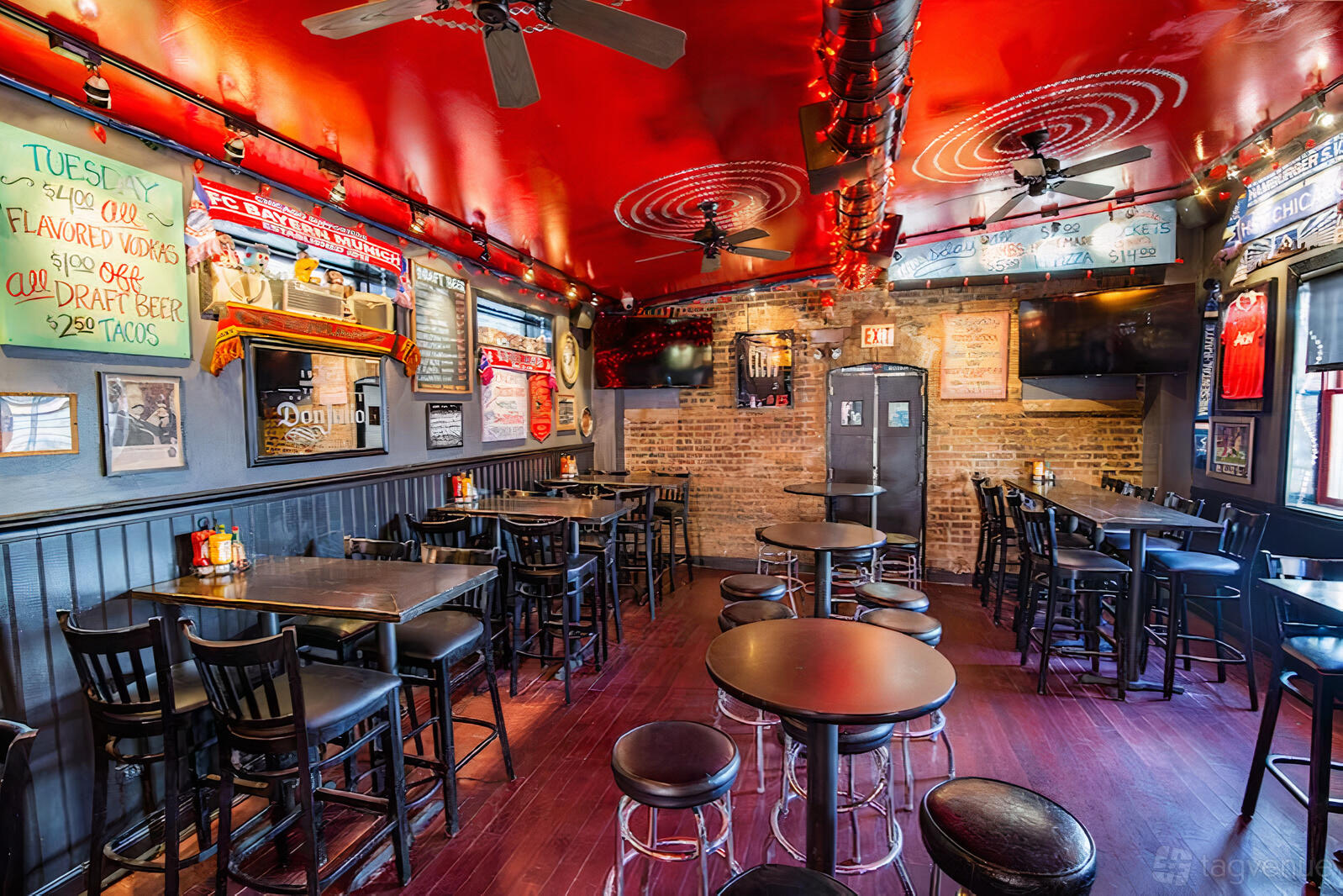 A bar with exposed brick walls, high-top tables, colorful chalkboard menus, and red painted ceiling at Cleos.