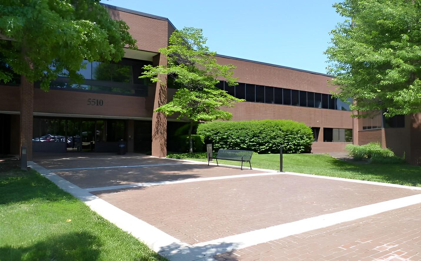 A coworking space with a brick exterior, large windows, and landscaped greenery at Perfect Office Solutions - Alexandria.