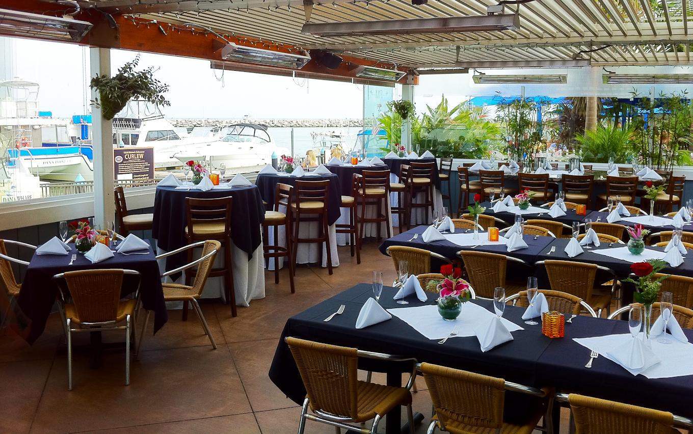 An outdoor restaurant patio with marina views, arranged tables with black linens and white napkins at Proud Mary's Restaurant.