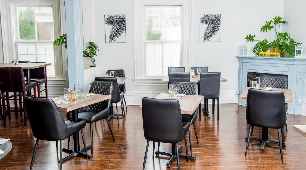 An event space in a restaurant with dark leather chairs, wooden floors, decorative fireplace, and large sunny windows at Laz Authentic Cuisine Inc.