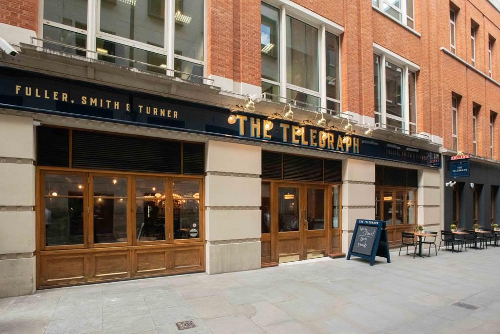 A pub with wood-framed windows, brick facade, and outdoor seating area at The Telegraph.