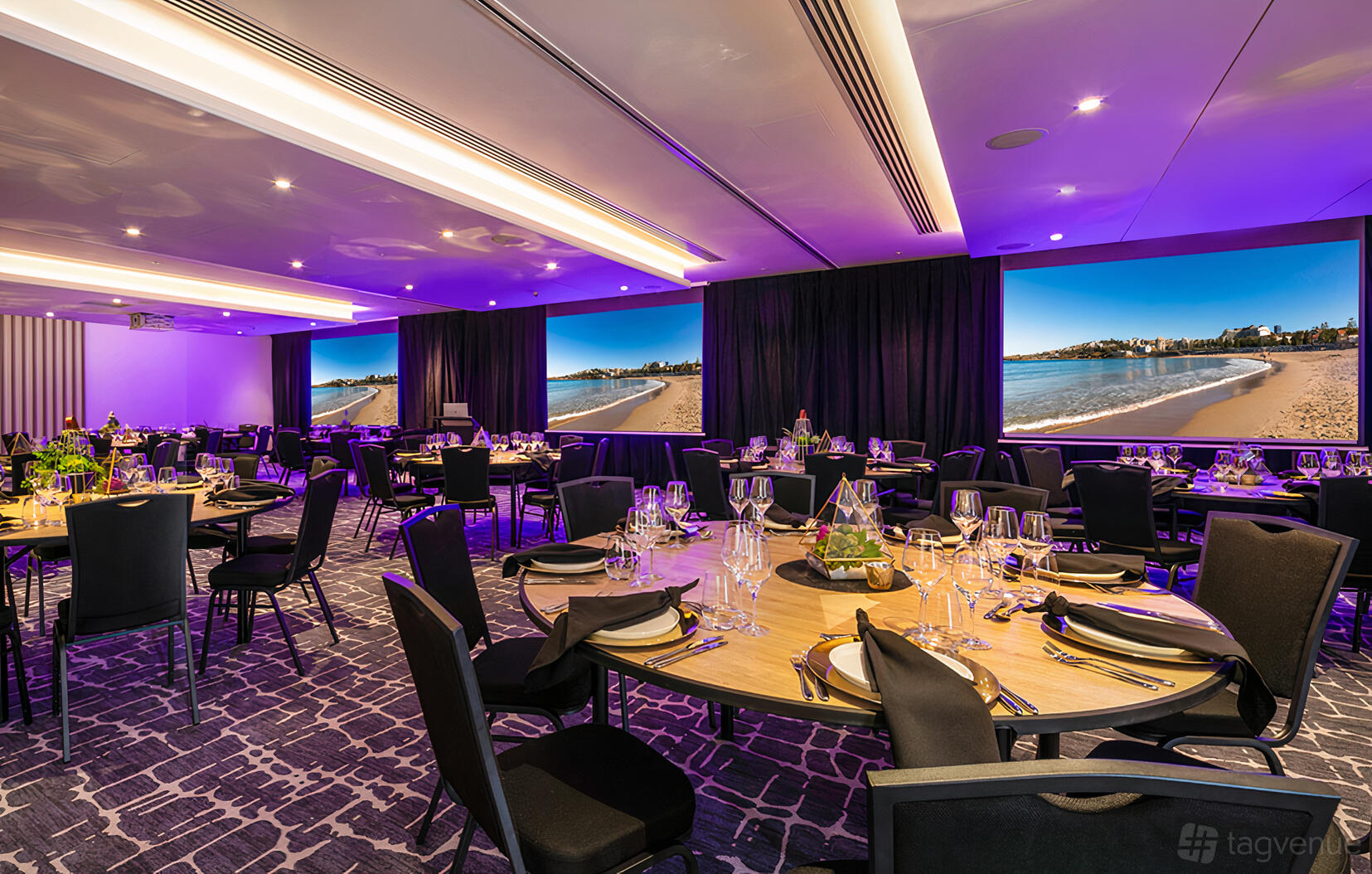 An event space with round tables set with glassware and beachside mural walls at Crowne Plaza Sydney Coogee Beach.