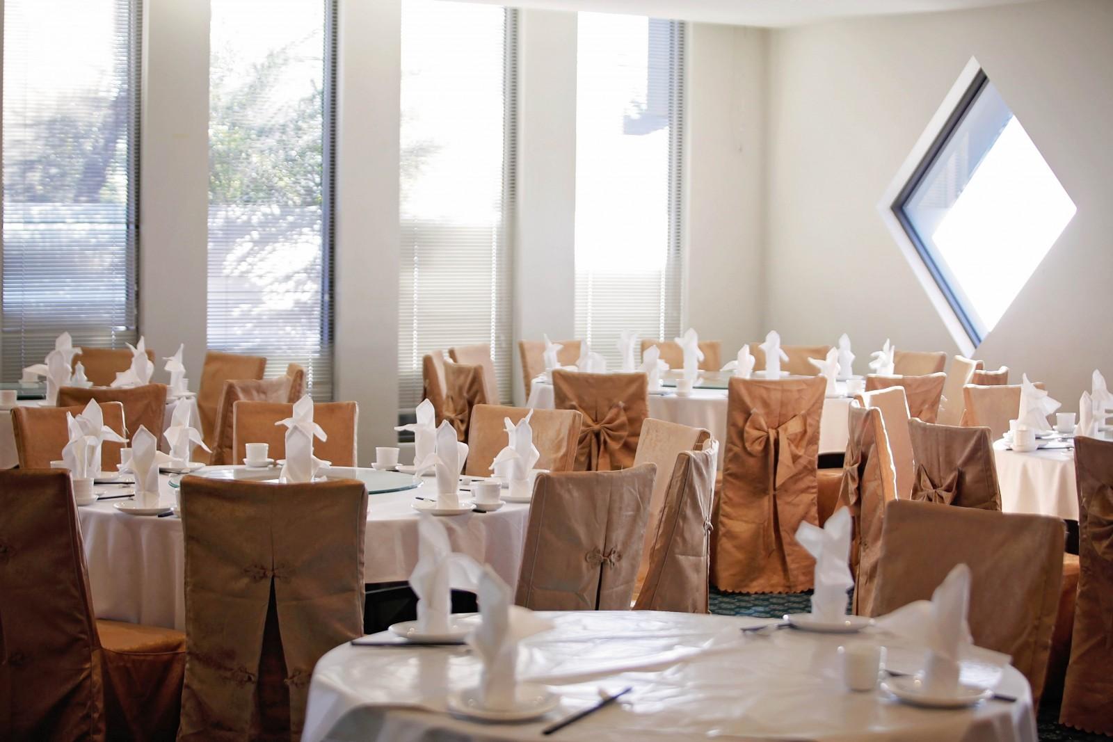 An event space with round tables set with white linens, folded napkins, and large windows at Golden Pebble Hotel