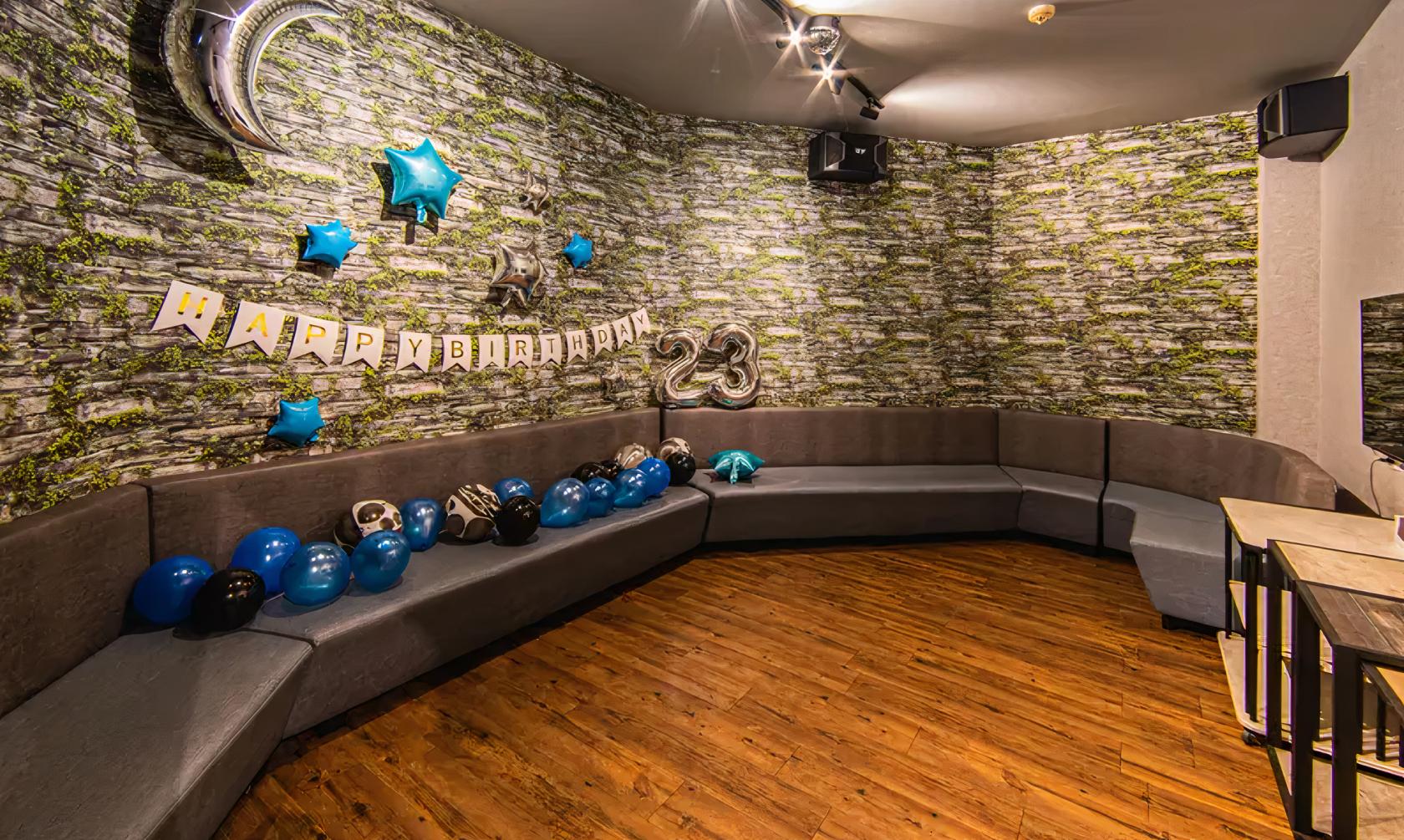 An event space with curved gray seating, wood floors, balloon decorations, and birthday banners at 7th Heaven KTV Cafe.