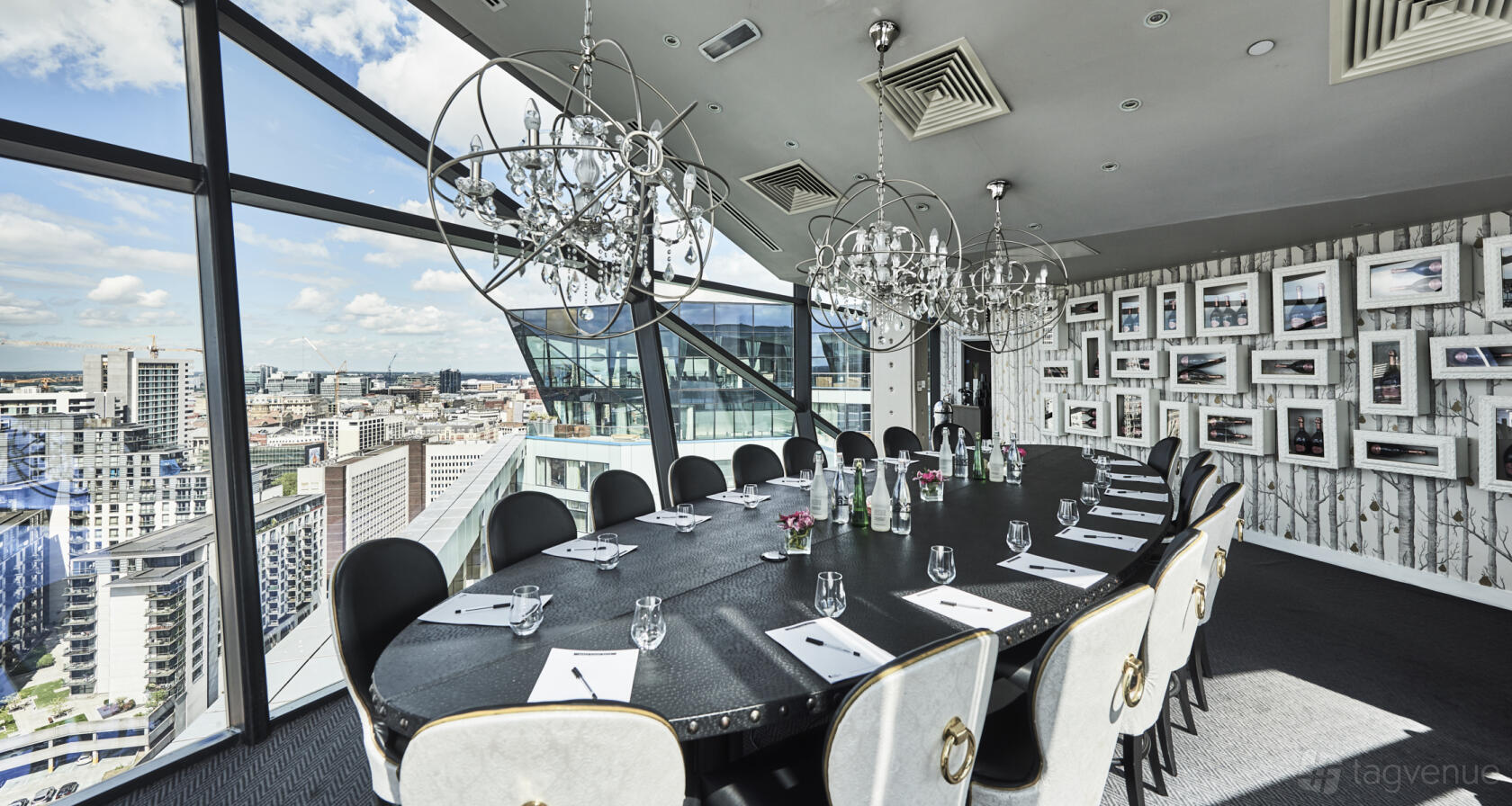 A dining room with floor-to-ceiling windows, city views, chandeliers, and a long oval table at The Cube.
