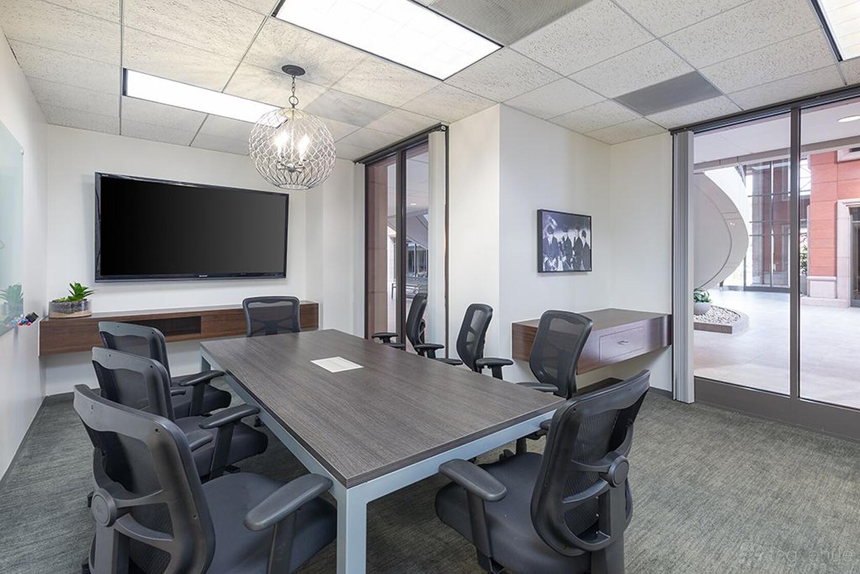 A coworking space with a rectangular conference table, ergonomic chairs, wall-mounted TV, and glass doors at Premier Workspaces - 23 Corporate Plaza.
