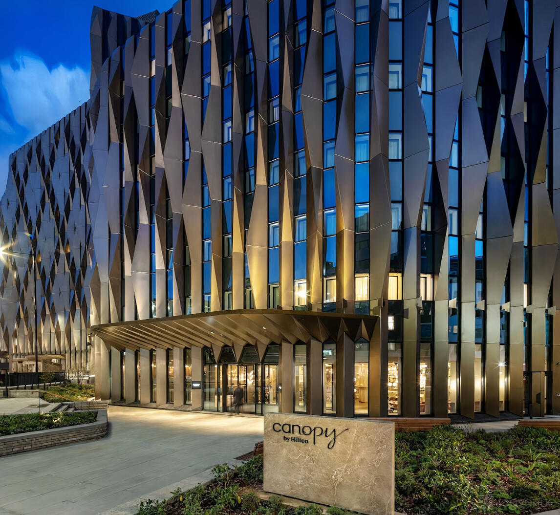 A hotel with a geometric metal facade and large illuminated windows at Canopy by Hilton London City.