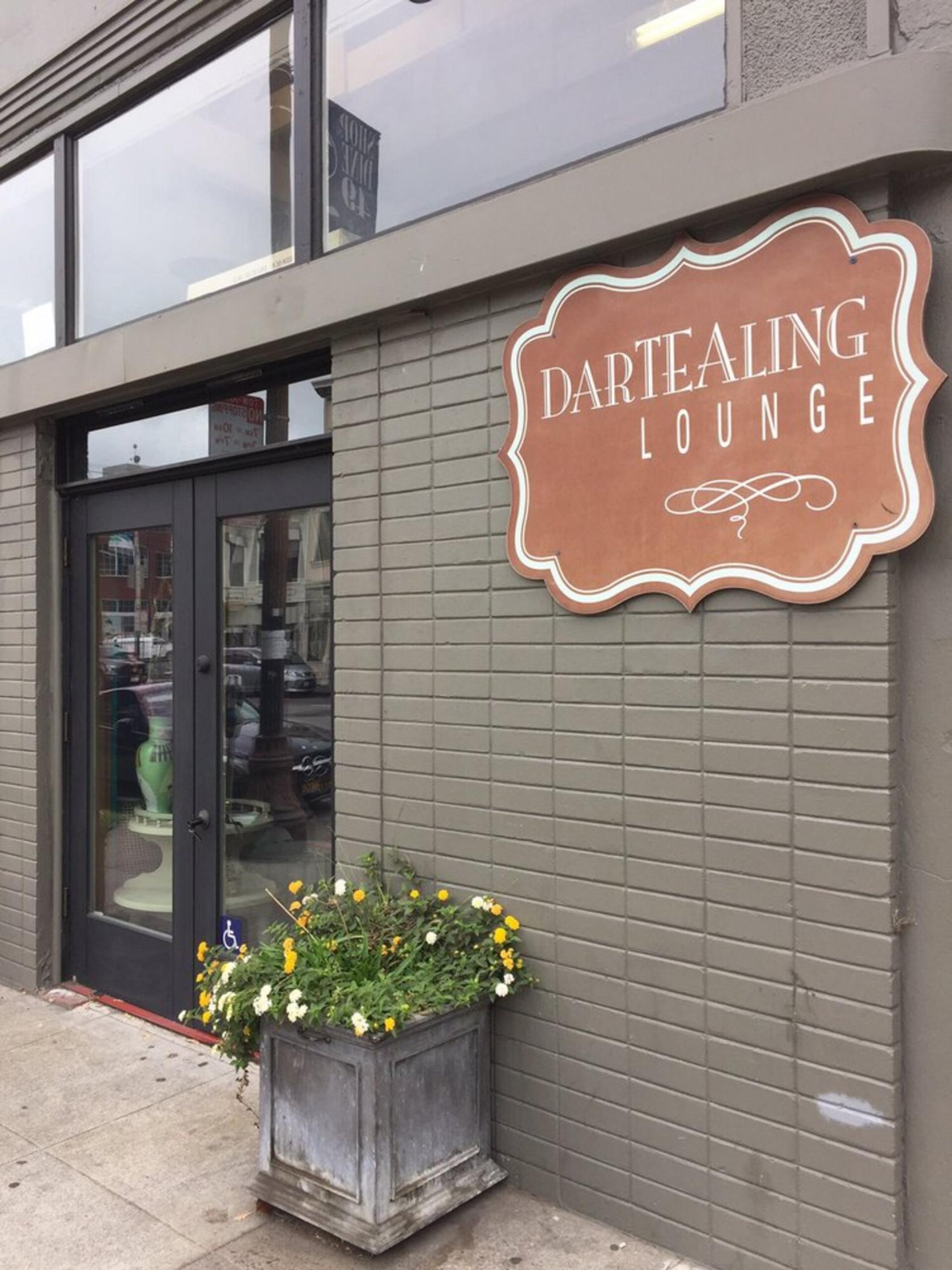 A café entrance with glass double doors, potted flowers, and a large hanging sign at Dartealing Lounge.