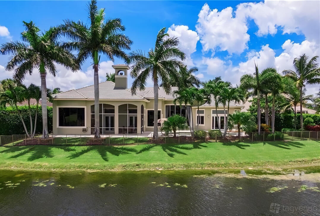 A country house surrounded by palm trees, large windows, and a fenced lawn overlooking a pond at Savvy Ventures Studios.
