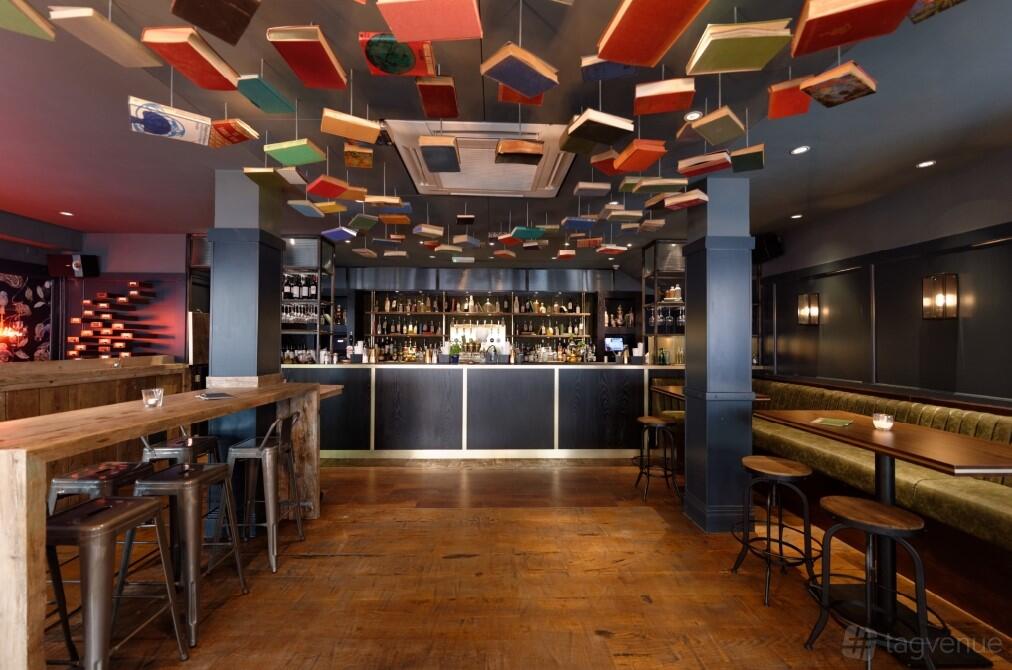 A cocktail bar with books suspended from the ceiling, wooden floors, and a long counter at Clerkenwell and Social.