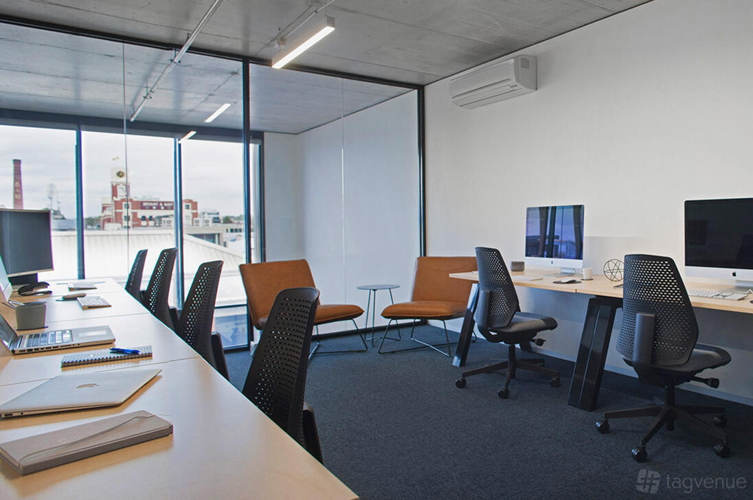 An office space with workstations, ergonomic chairs, computers, and large windows at collective_100.