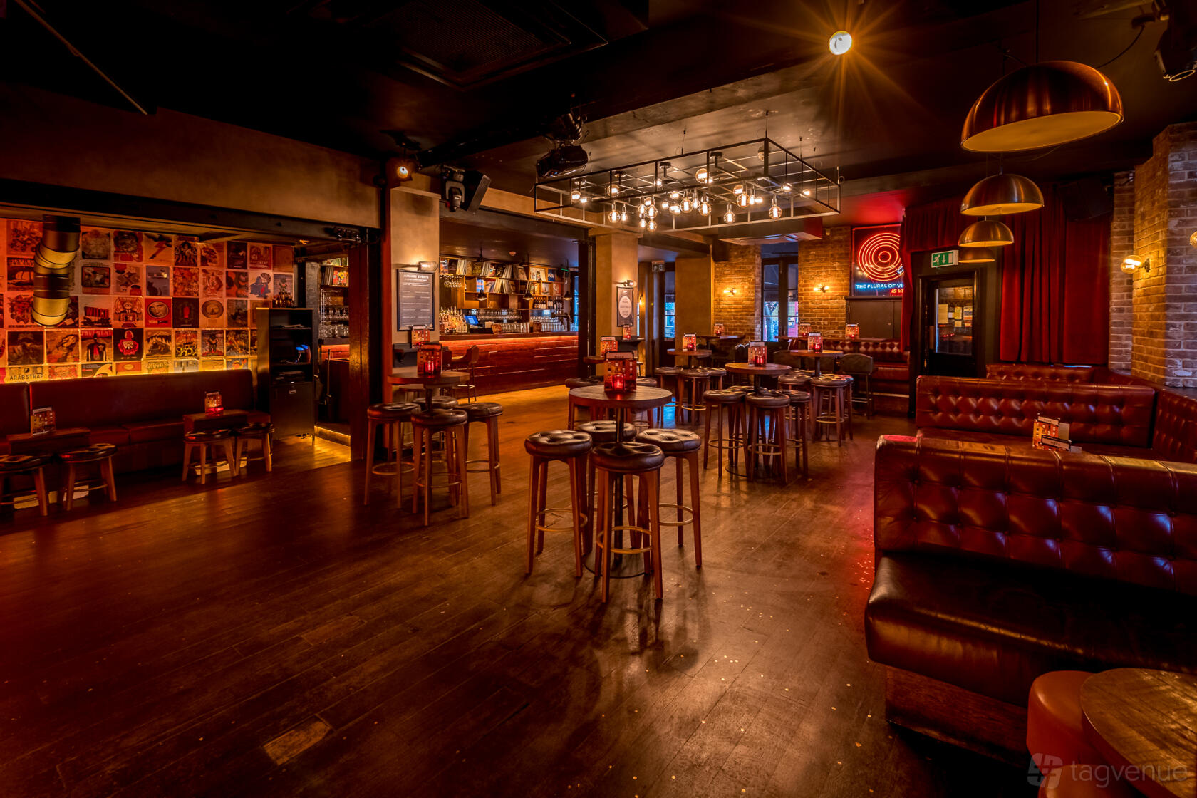 A bar with high tables, exposed brick walls, leather banquette seating, and warm pendant lighting at Northcote Records.