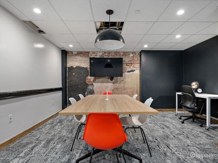 A meeting room with a wooden conference table, mix of white and orange chairs, wall-mounted TV, and exposed brick detail at 25N Coworking Waco.