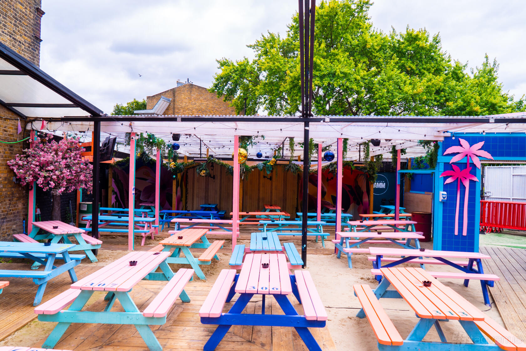 An outdoor nightclub area with colorful picnic tables, sandy flooring, and string lights at Brixton Jamm.