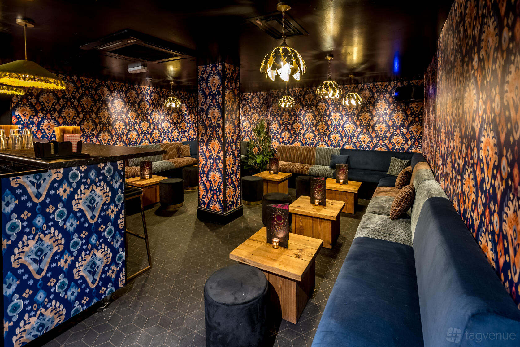 An event space in a cocktail bar with patterned wallpaper, velvet seating, and wooden tables at The Cocktail Club Oxford Circus.