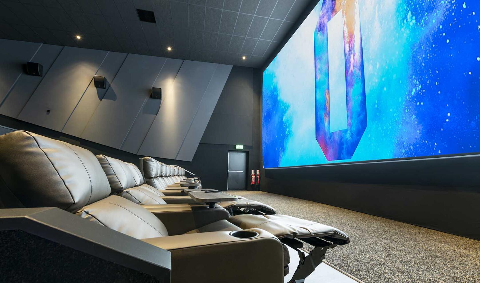 A cinema with reclining leather seats and a large screen displaying a colorful graphic at ODEON LUXE Leeds Thorpe Park.
