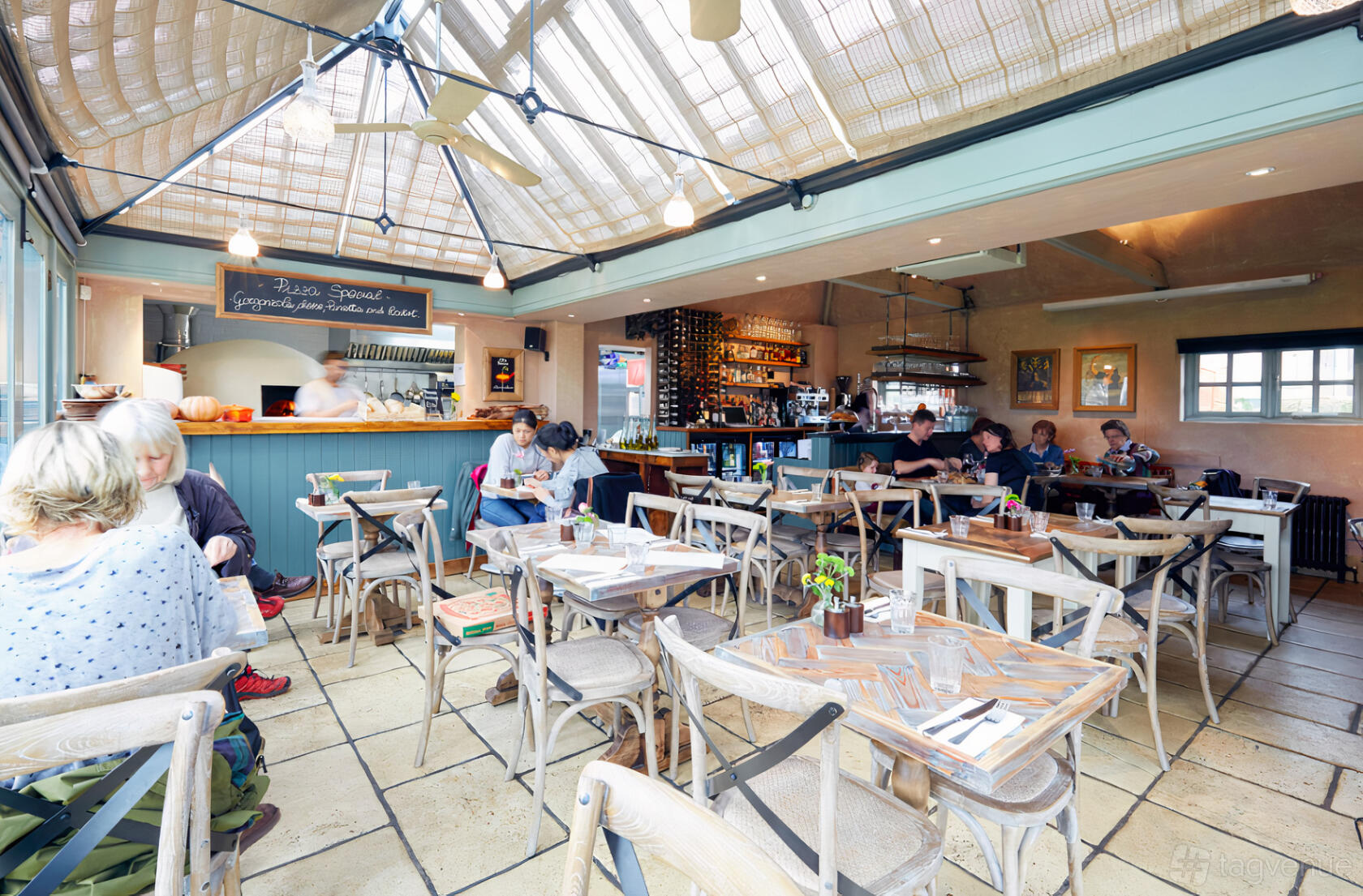 A restaurant with wooden tables, cross-back chairs, a skylight ceiling, and an open kitchen at Arthur's.