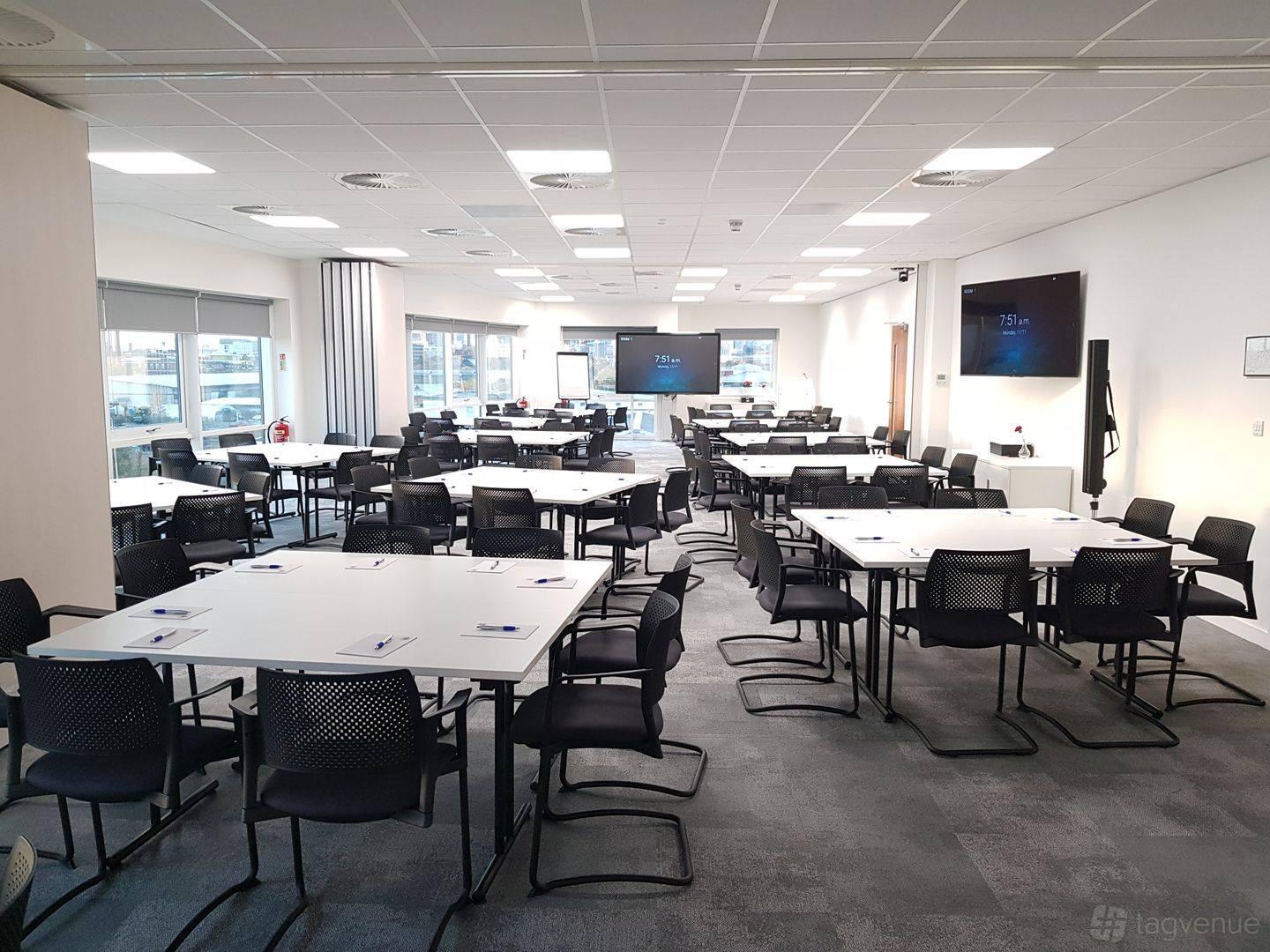 An event venue with large windows, multiple white tables, black chairs, and built-in screens at ABDO National Resource Centre.