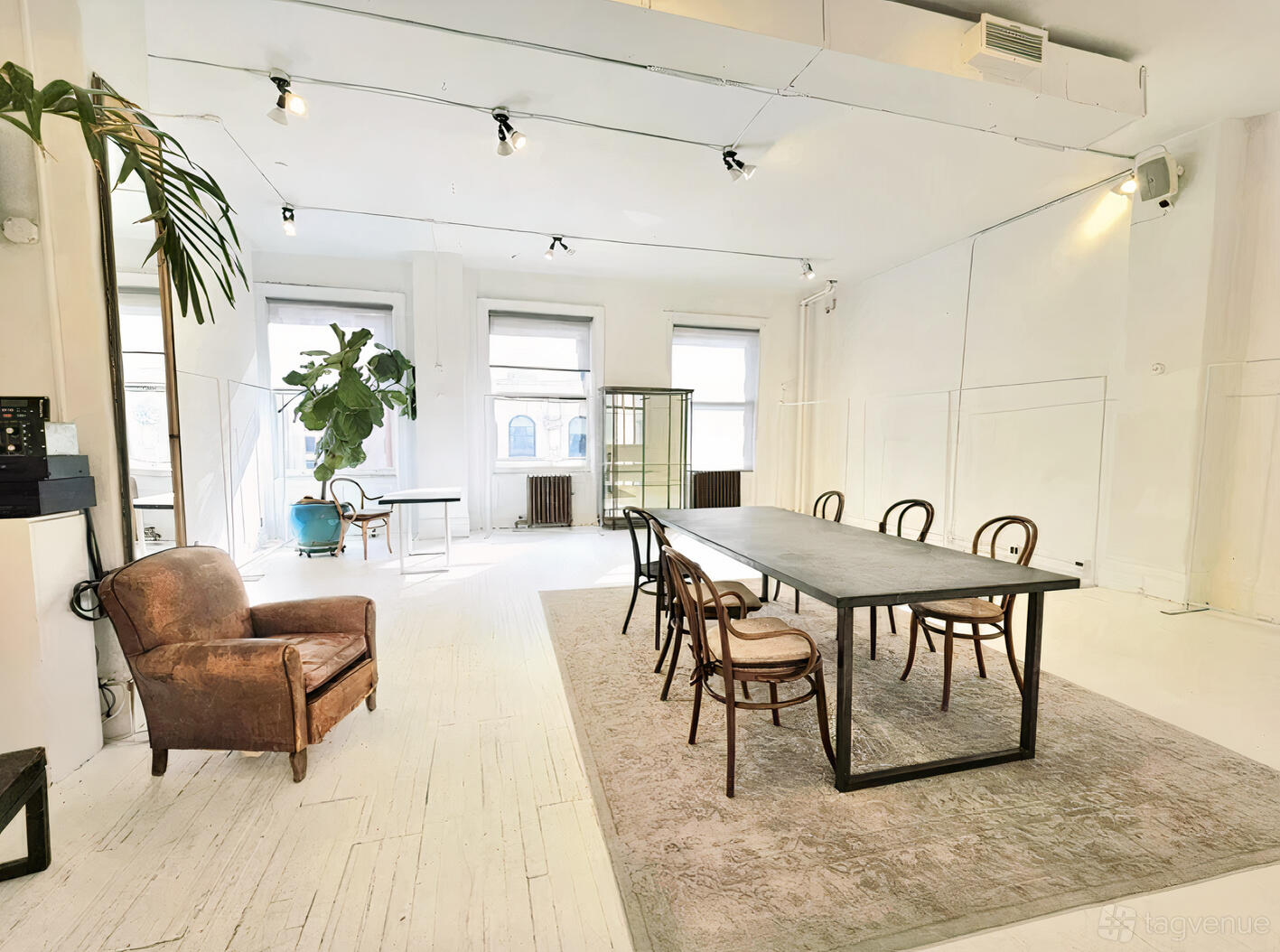 An event venue with large windows, white walls, wooden chairs around a long table, and a vintage leather armchair at Apropo Showroom.