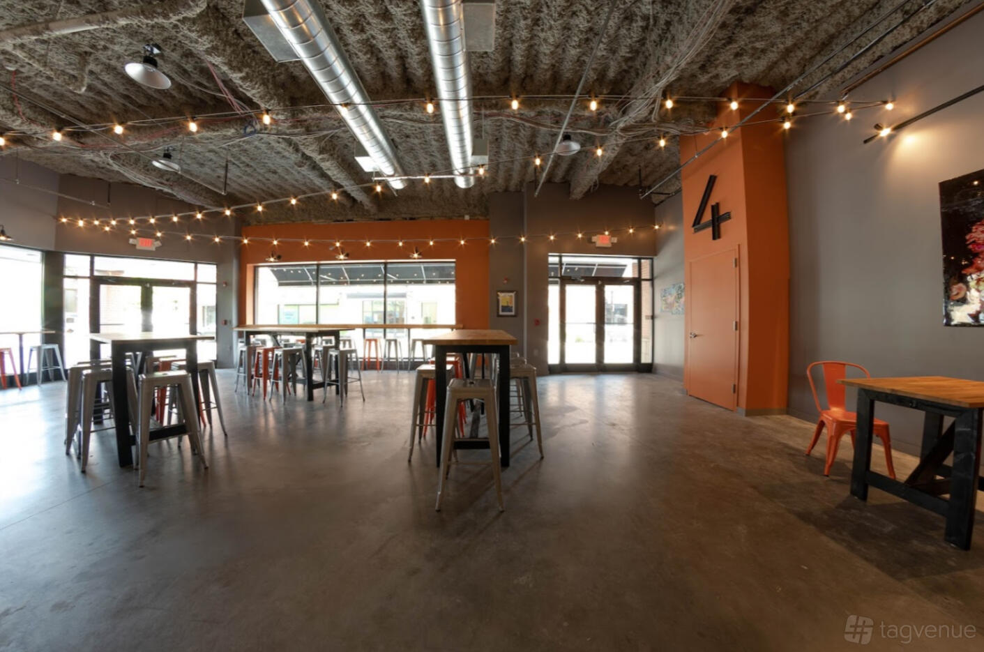 An industrial event venue with tall ceilings, string lights, and high-top tables at Four City Brewing Company.
