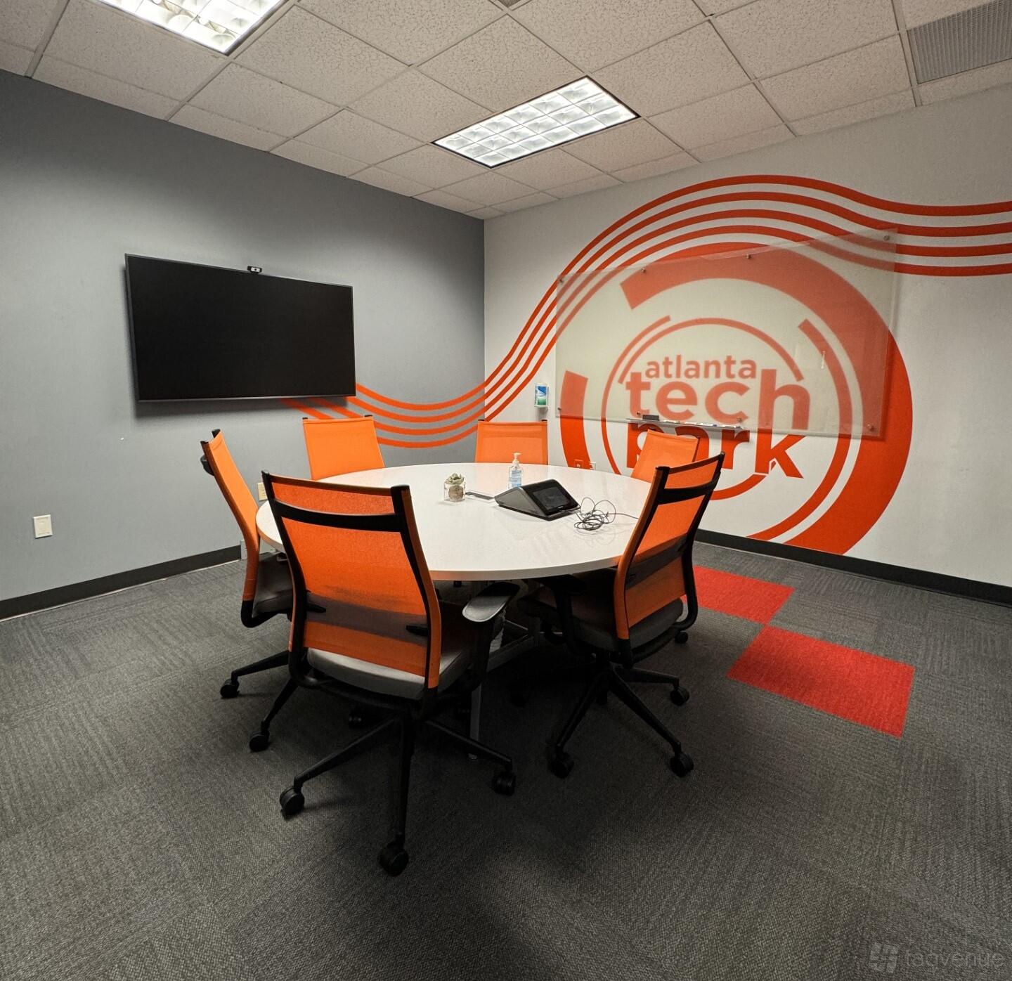 A meeting room with orange chairs, a round white table, wall-mounted screen, and branded wall graphics at Atlanta Tech Park.