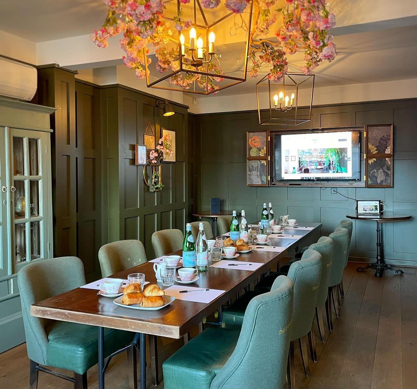 A bar dining room with olive green paneled walls, a long wooden table set for a meeting, and floral ceiling decor at The Lost and Found Sheffield.