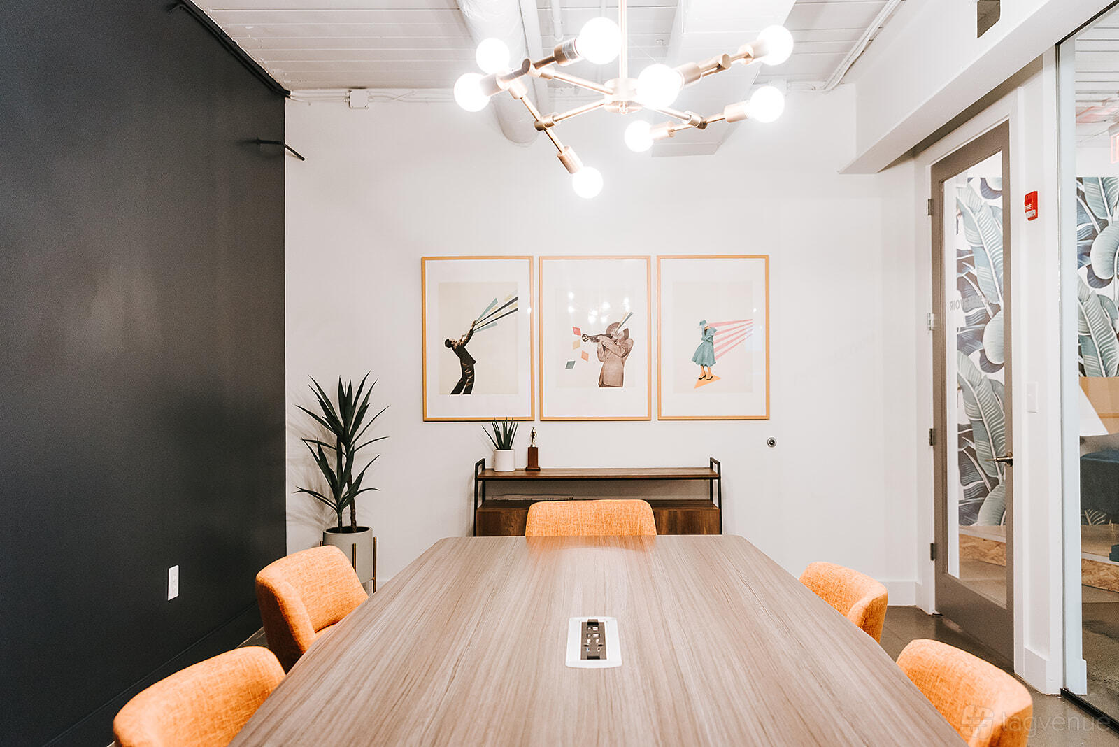 A meeting room with a wooden table, orange chairs, modern chandelier, and framed animal art at THRIVE - Alpharetta.