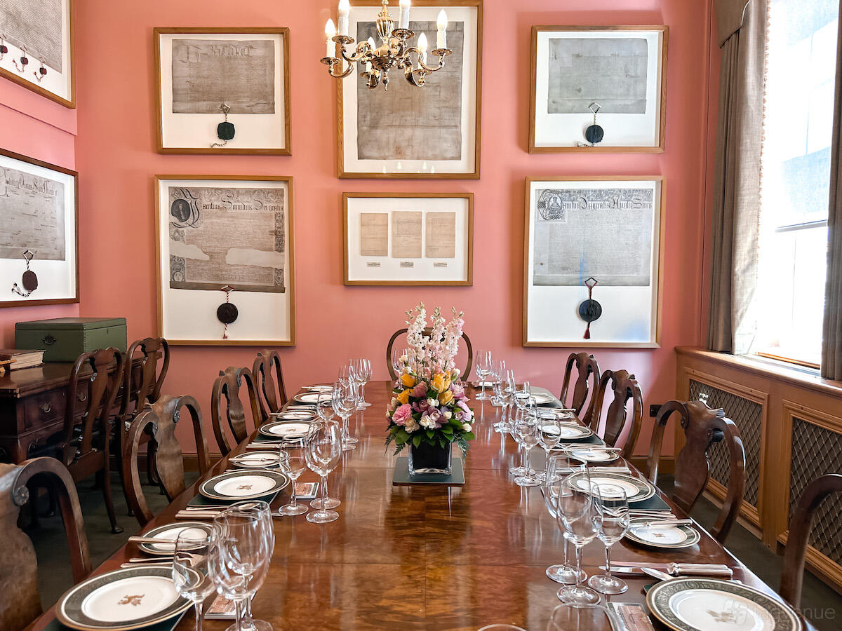 An event space in a hall with a polished wood dining table, floral centerpiece, and framed historical documents at Barber-Surgeons’ Hall.