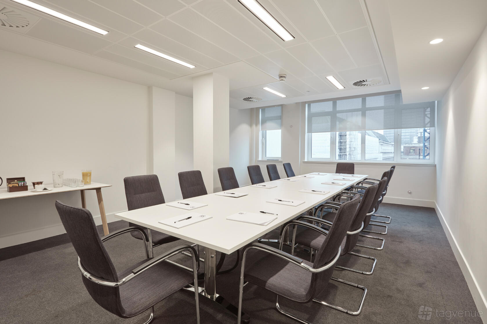 A meeting room with a long white conference table, black chairs, large windows, and notepads at 18 Smith Square.