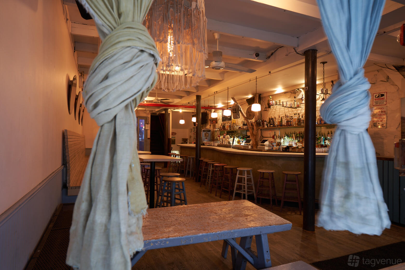 A bar with a long counter, wooden stools, exposed brick, and pendant lighting at Piano's.