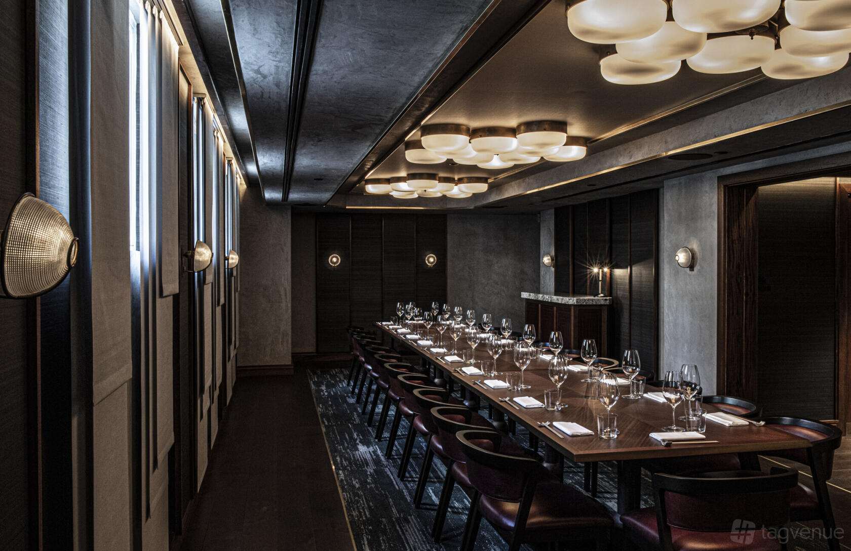 A dining room with long wooden tables, dark chairs, and modern ceiling lights at Lucky Cat.